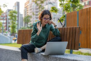 Woman waving at a computer in a garden bench. Vrouw zwaait naar een computer in een tuinbank.